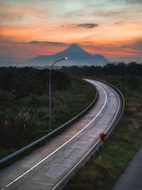 Railroad tracks by road against sky during sunset