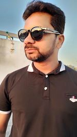 Portrait of young man wearing sunglasses standing against sky
