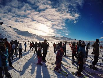 People skiing on snow covered field against sky