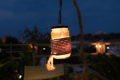 Close-up of illuminated lighting equipment hanging on tree against sky at night