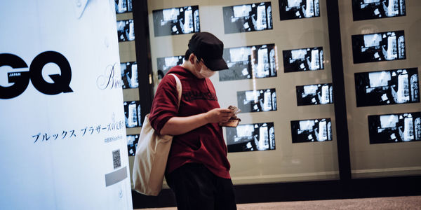 Side view of woman using phone while standing against wall