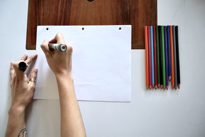 Cropped image of person holding paper against colored pencils