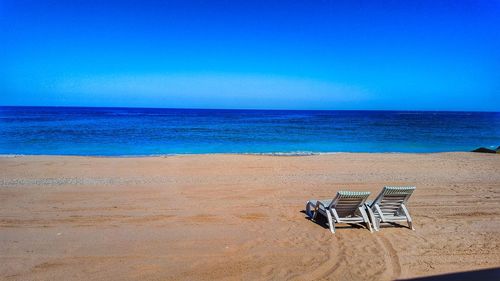 Chairs on beach against clear blue sky