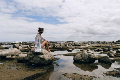 Woman standing on rock by sea against sky