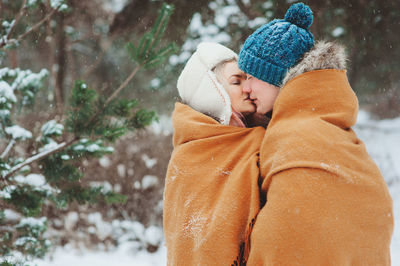 Woman kissing man while wearing warm clothing during winter