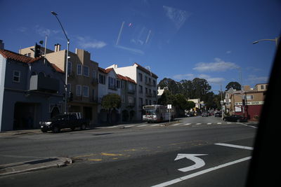 Cars on road by buildings in city against sky