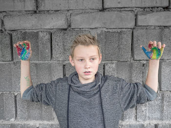 Cute boy with painted hands standing against stone wall