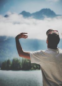 Rear view of man with arm outstretched standing against sky