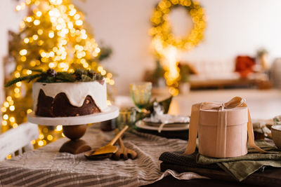 Festive christmas cake on a wooden stand on a set dining table and a round gift box