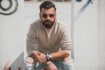 Young man wearing sunglasses sitting against wall