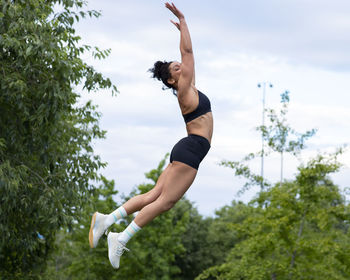 Side view of black female athlete in activewear in moment of jumping above ground during intense workout in park