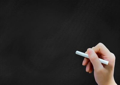 Close-up of hand holding cigarette over black background