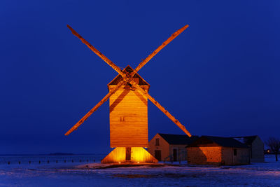 Traditional windmill by sea against clear blue sky