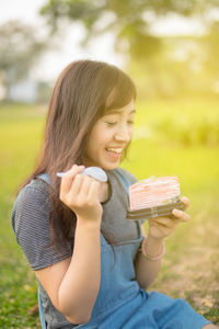 Smiling young woman holding pastry while sitting on field at park