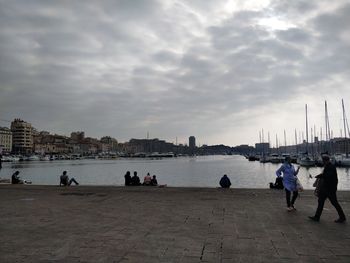 People on sidewalk by buildings in city against sky