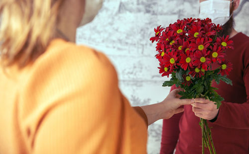 Midsection of couple holding bunch of red flowers during pandemic