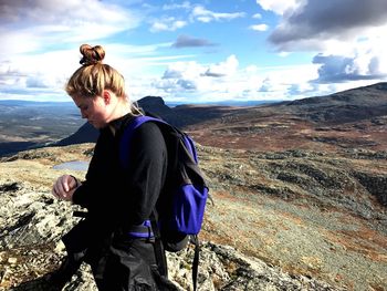 Rear view of young woman standing on mountain against sky