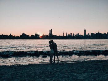 Silhouette man standing by sea against clear sky during sunset