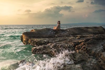 Man sitting on rock at beach against sky