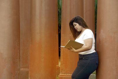 Young woman reading book by columns 