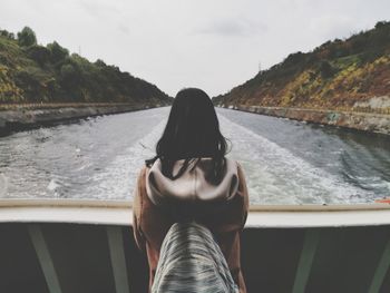 Rear view of woman in boat on river against sky