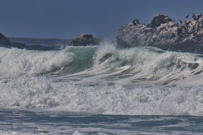 Waves splashing in sea against clear sky