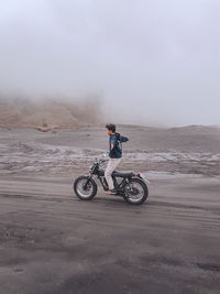 Man riding motorcycle on sand against sky