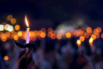Defocused image of hand holding illuminated christmas lights at night