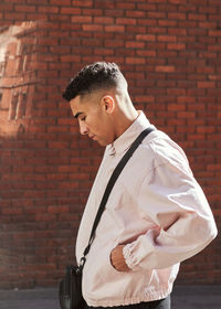 Side view of young man standing against brick wall