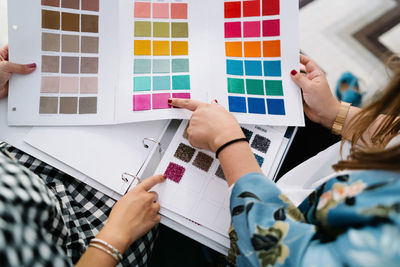 Top view of unrecognizable female designers standing at table in bright studio and choosing color of textile samples