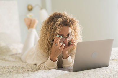 Young woman using mobile phone while sitting on bed at home