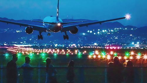 People looking at airplane against sky at night