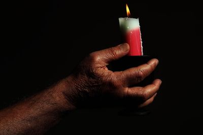 Close-up of hand holding burning candle against black background