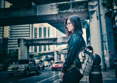 Side view of woman standing on sidewalk in city