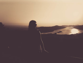 Rear view of man looking at sea against sky during sunset