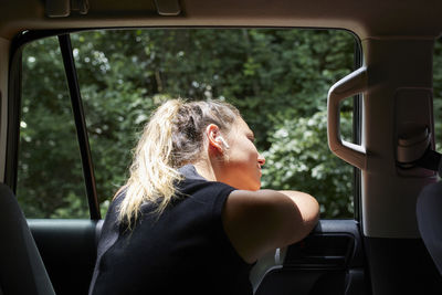 Young blond woman leaning out car window listening music with headphones