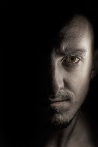 Close-up portrait of serious young man against black background