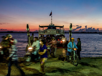 People on bicycle in city against sky during sunset