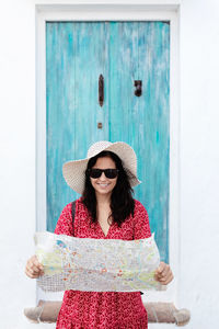 Portrait of smiling young woman standing against door