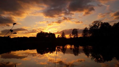 Reflection of silhouette trees in lake against sky during sunset