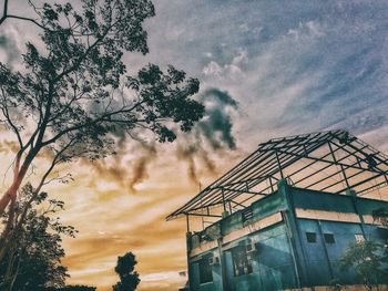 Low angle view of silhouette tree by building against sky