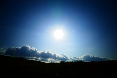 Low angle view of sun shining over silhouette mountain