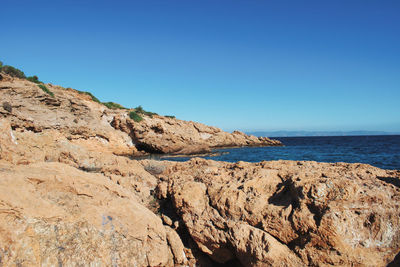 Rock formation on beach against clear blue sky