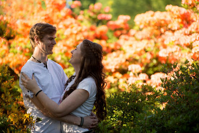 Side view of cheerful couple standing against flowers at park