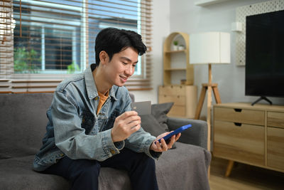 Young man using mobile phone while sitting at home