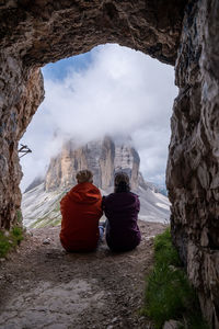 Rear view of people sitting on rock against sky