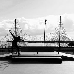 Man skateboarding at park by bridge against lake