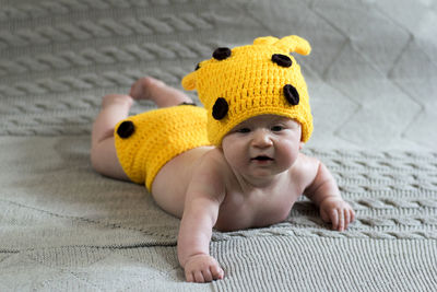 Full length of cute baby girl wearing yellow knit hat on bed