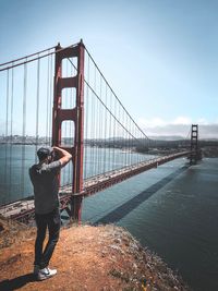 Rear view of man standing by bridge against sky