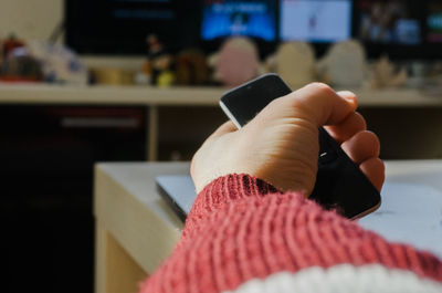 Cropped hand of woman holding mobile phone at home